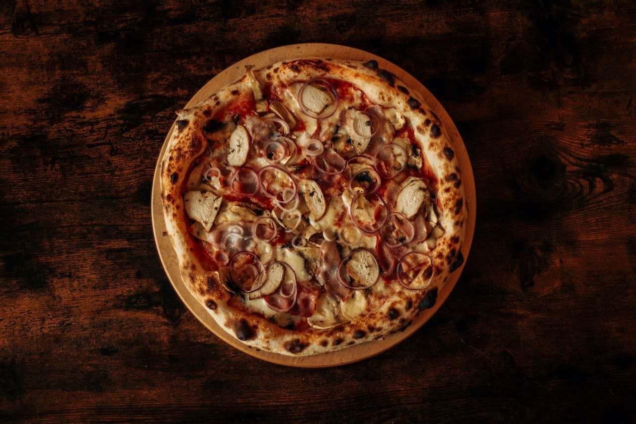 Close-up of a freshly baked pizza with onions, mushrooms, and cheese on a dark rustic wooden table.