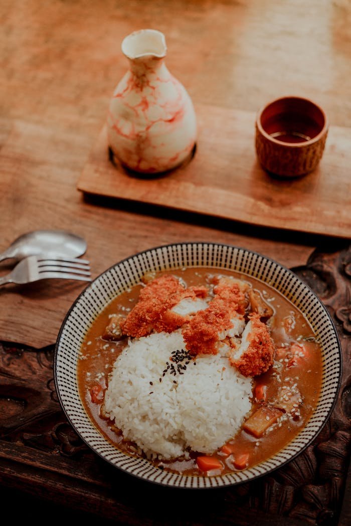 Japanese curry rice with breaded chicken served with sake set on a rustic wooden table.