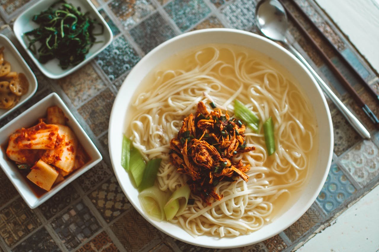 Top view of a Korean noodle soup with various side dishes, emphasizing Asian cuisine.