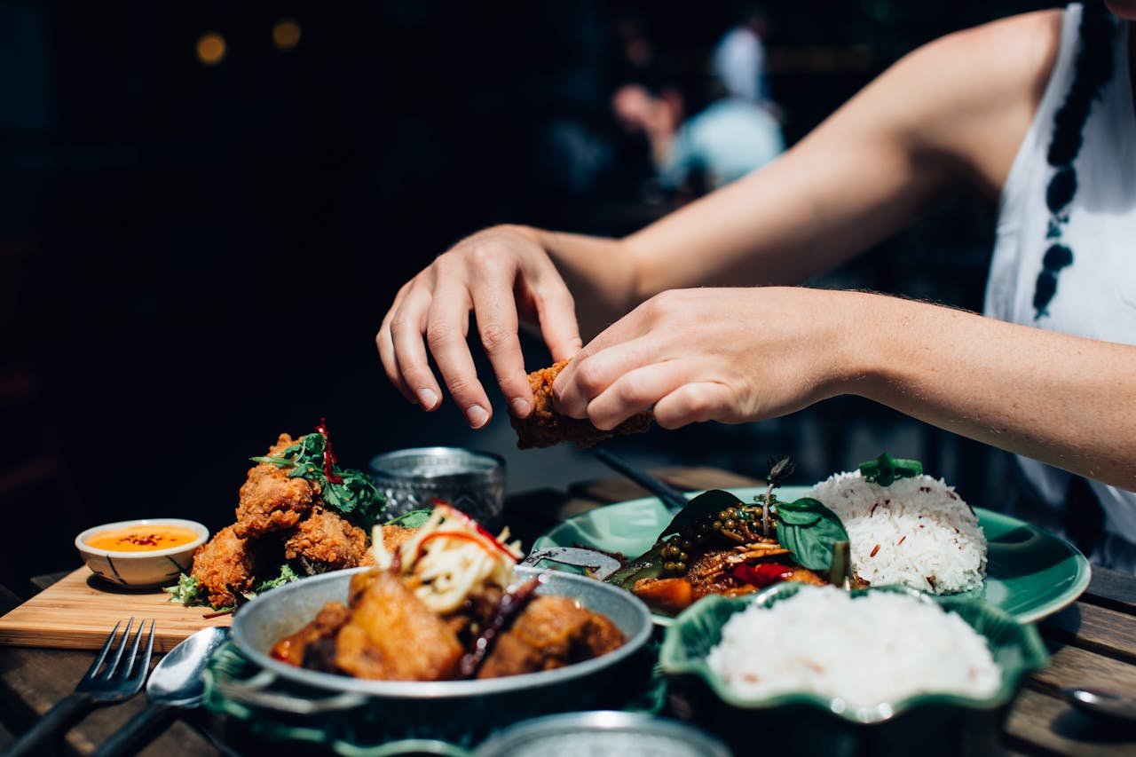Close-up of a womans hands enjoying fried chicken and rice outdoors in a restaurant setting.
