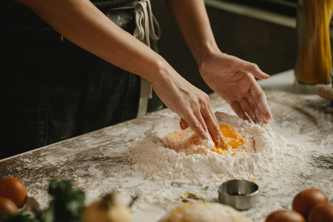Hands kneading dough with eggs and flour for homemade pasta in a kitchen setting.